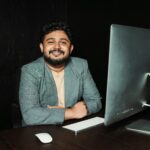 Confident businessman sitting at desk, working on computer in modern office.